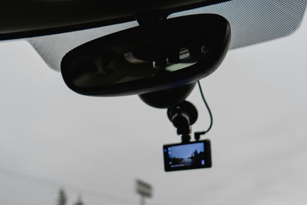 A dash camera mounted on the windshield behind a car's rear-view mirror