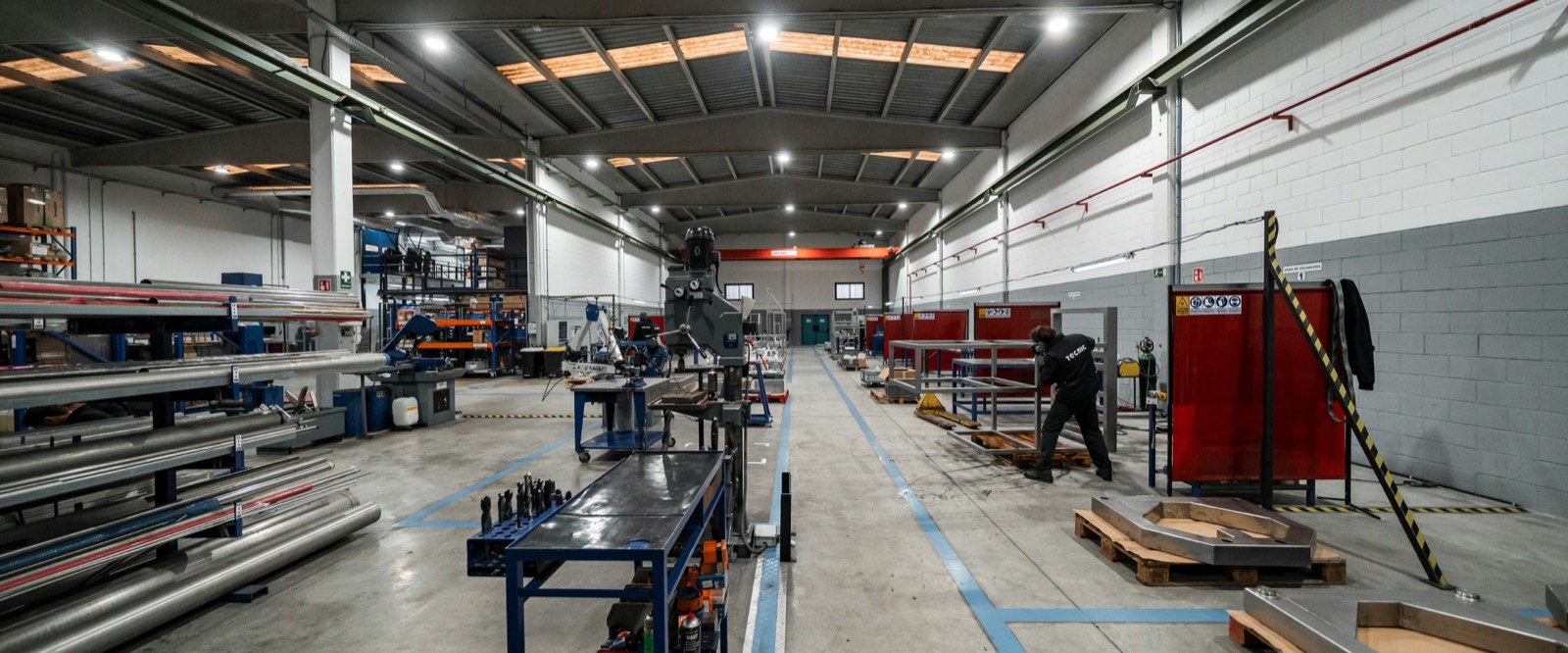 The inside of a working manufacturing plant, with benches, materials and staff down a long aisle