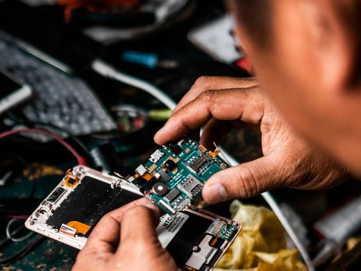 Hands working on a circuit board at a cluttered electronics repair bench